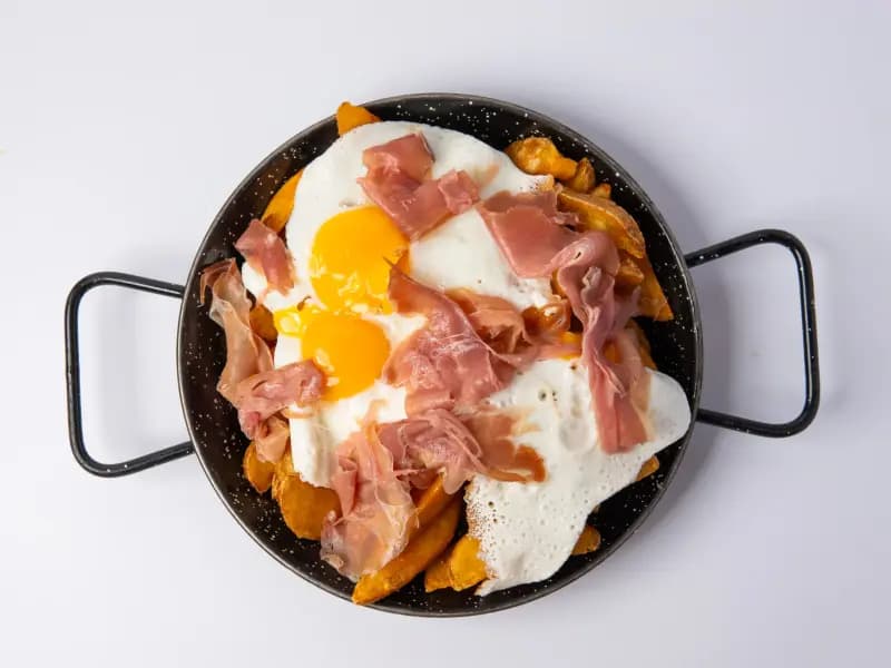 Huevos rotos con jamón serrano en sartén